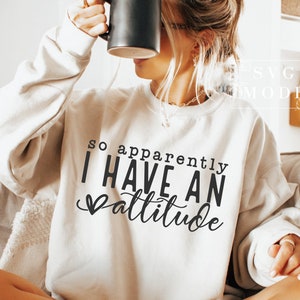 May include: A white sweatshirt with the text "so apparently I HAVE AN attitude" in black lettering with a small heart before the word "attitude".