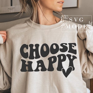 Peut inclure: Un sweat-shirt beige avec le texte "CHOOSE HAPPY" en lettres noires de style rétro avec un petit cœur noir.