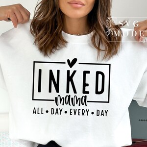 May include: White sweatshirt with black text that reads "INKED mama ALL DAY EVERY DAY" with a small heart above the word "INKED".