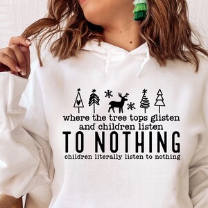 K&ouml;nnte beinhalten: Wei&szlig;er Hoodie mit einem schwarzen Grafikdesign mit einem Weihnachtsbaum, einem Rentier und Schneeflocken. Der Text lautet "where the tree tops glisten and children listen to nothing, children literally listen to nothing."