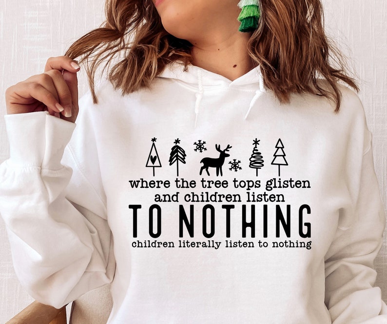 K&ouml;nnte beinhalten: Wei&szlig;er Hoodie mit einem schwarzen Grafikdesign mit einem Weihnachtsbaum, einem Rentier und Schneeflocken. Der Text lautet "where the tree tops glisten and children listen to nothing, children literally listen to nothing."