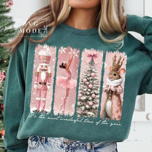 K&ouml;nnte beinhalten: Ein t&uuml;rkisfarbener Pullover mit einem weihnachtlichen Design, das einen Nussknacker, eine Ballerina, einen Weihnachtsbaum und eine Maus mit Krone zeigt. Der Text "It's the most wonderful time of the year" ist auf dem Pullover aufgedruckt.