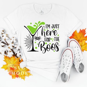 May include: White t-shirt with a green cocktail glass, spider web, and the text "I'm just here for the boos" in black and green.
