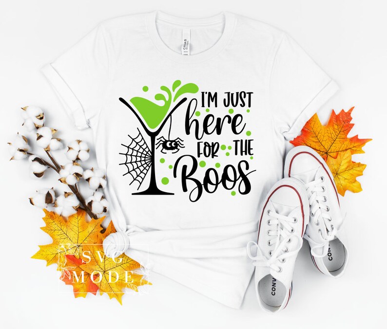May include: White t-shirt with a green cocktail glass, spider web, and the text "I'm just here for the boos" in black and green.