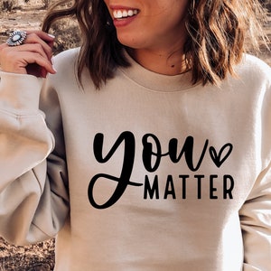 May include: A beige sweatshirt with the text "you matter" in black lettering with a small heart symbol.