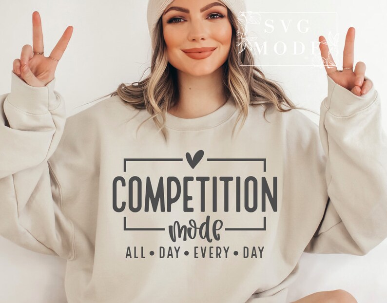 May include: A beige sweatshirt with the text "COMPETITION mode ALL DAY EVERY DAY" in black lettering. A small heart is above the word "COMPETITION".