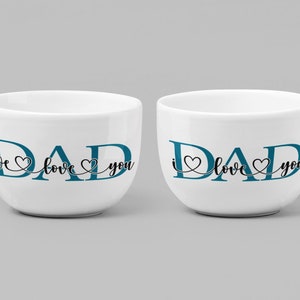 Puede incluir: Dos tazas de cer&aacute;mica blanca con texto azul que dice "DAD we love you" y "DAD i love you".