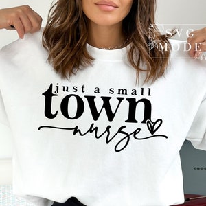 May include: White sweatshirt with black text that reads "just a small town nurse" with a small heart graphic.