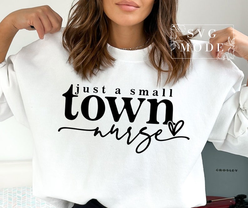 May include: White sweatshirt with black text that reads "just a small town nurse" with a small heart graphic.
