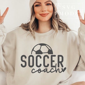 May include: A beige sweatshirt with a black football graphic and the text "SOCCER coach" with a small heart.