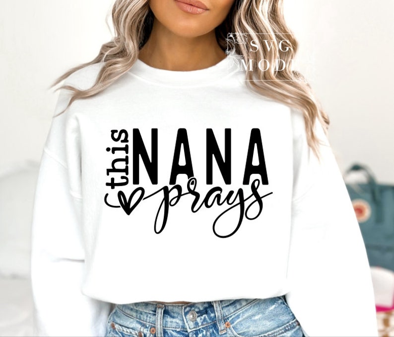 May include: White sweatshirt with black text that reads "This Nana prays" with a heart symbol.