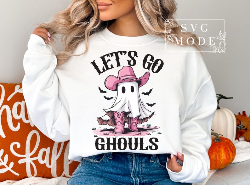Może przedstawiać: Biała bluza z nadrukiem ducha w r&oacute;żowym kowbojskim kapeluszu i butach. Na bluzie widnieje napis "Let's Go Ghouls".