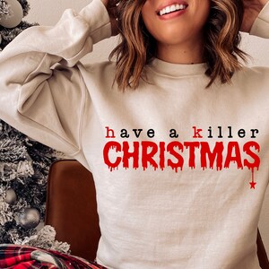 May include: A beige sweatshirt with the phrase "have a killer CHRISTMAS" printed in red and black. The word "CHRISTMAS" has a dripping blood effect. A star is dripping from the letter "S".