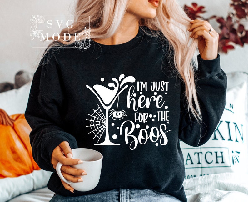 May include: Black sweatshirt with a white graphic design of a martini glass with a spider hanging from it and the text "I'm just here for the boos".