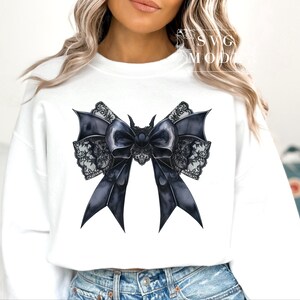May include: A white sweatshirt with a black and white lace bow with a black center. The bow has a gothic style.