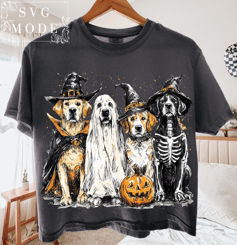 May include: Dark gray t-shirt featuring four dogs dressed in Halloween costumes. One dog is a ghost, another is a skeleton, and two wear witch hats and capes. A carved pumpkin sits in front of the dogs.