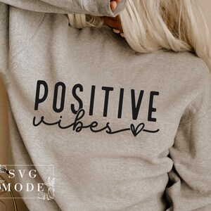 Peut inclure: Un sweat-shirt gris avec le texte "POSITIVE vibes" en lettres noires et un petit symbole de c&oelig;ur.