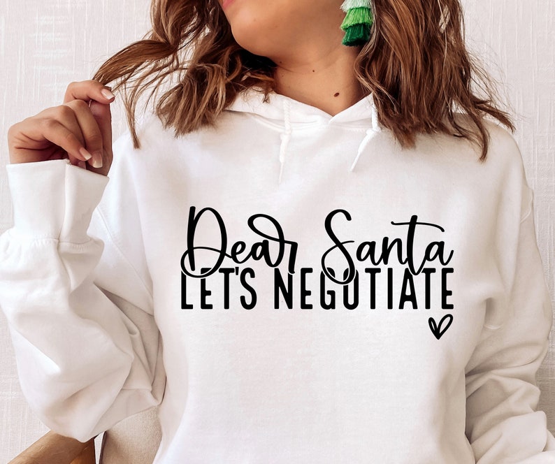 Pode incluir: Camisola de moletom branca com capuz com o texto "Caro Papai Noel, vamos negociar" em fonte de escrita cursiva preta com um pequeno s&iacute;mbolo de cora&ccedil;&atilde;o.