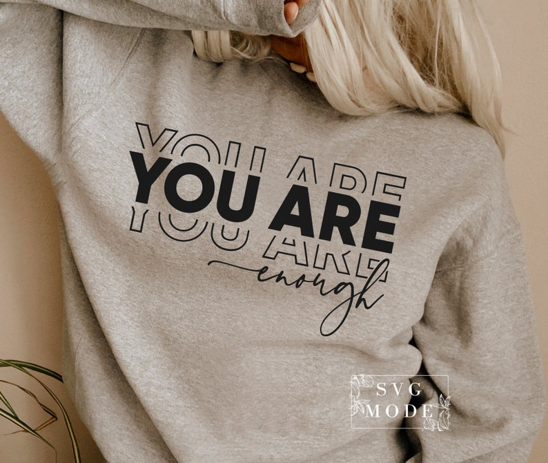 May include: A gray sweatshirt with the text "YOU ARE enough" printed in black. The text is stacked and stylized with overlapping letters.