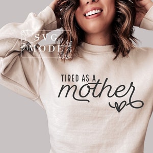 May include: A beige sweatshirt with the text "Tired as a mother" in black cursive lettering with a small heart at the end.