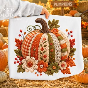May include: A white sweatshirt featuring a large, detailed graphic of a pumpkin with textured panels in orange, green, and cream. The pumpkin is decorated with embroidered floral patterns, lace-like textures, and autumn leaves, with the text SVG MODE.
