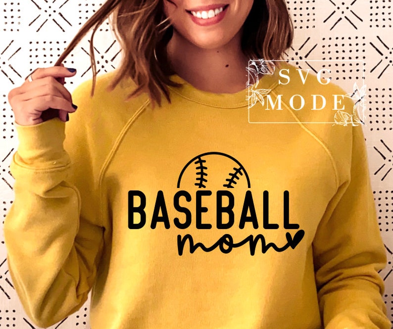 May include: Mustard yellow sweatshirt featuring a black baseball graphic and the words "BASEBALL mom". The design includes a baseball with stitching above the word "BASEBALL" and a heart replacing the "o" in "mom".