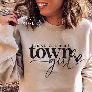 May include: A beige sweatshirt with the text "just a small town girl" printed on the front in black. A small heart is next to the text.
