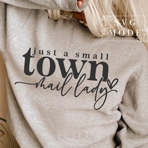 May include: A gray sweatshirt with the text "just a small town mail lady" in black lettering with a small heart.