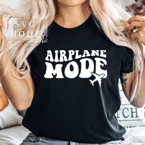 Puede incluir: Camiseta negra con texto blanco que dice "Airplane Mode" en una fuente retro. Un peque&ntilde;o gr&aacute;fico de avi&oacute;n est&aacute; debajo del texto.