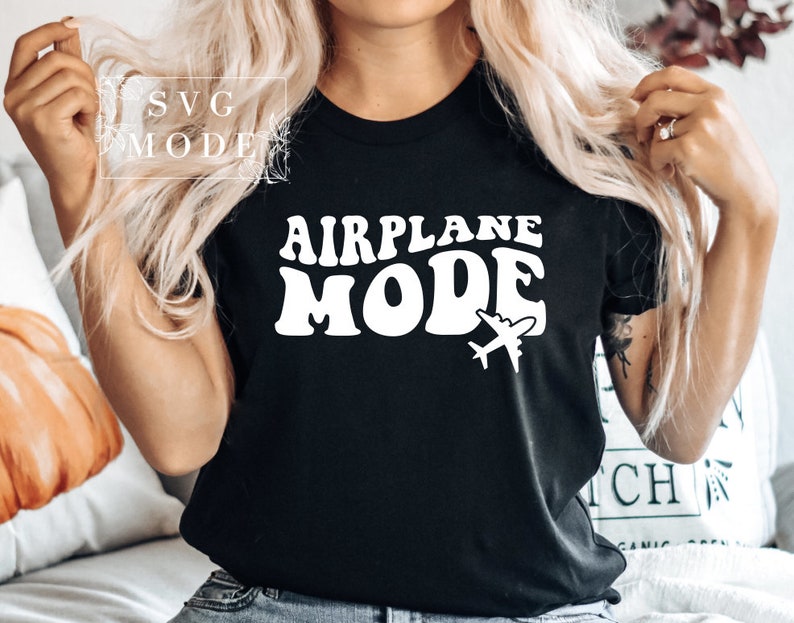 Puede incluir: Camiseta negra con texto blanco que dice "Airplane Mode" en una fuente retro. Un peque&ntilde;o gr&aacute;fico de avi&oacute;n est&aacute; debajo del texto.
