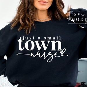 May include: Black sweatshirt with white text that reads "just a small town nurse" with a small heart after the word "nurse".