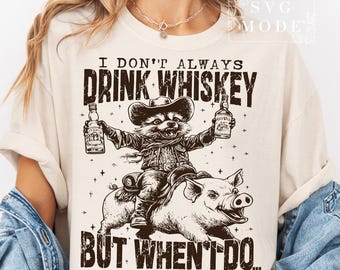 Puede incluir: Una camiseta beige con un diseño gráfico de un mapache con un sombrero de vaquero montando un cerdo. El texto en la camiseta dice "I don't always drink whiskey but when I do..."