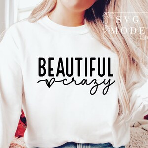 Pode incluir: Camisola branca de manga comprida com texto preto que diz "BEAUTIFUL crazy" com um pequeno s&iacute;mbolo de cora&ccedil;&atilde;o.