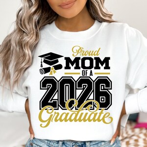Puede incluir: Sudadera blanca con el texto "Proud MOM of a 2026 Graduate" en negro y dorado. El dise&ntilde;o incluye un gorro de graduaci&oacute;n, un diploma y el a&ntilde;o 2026. La sudadera es de estilo c&oacute;modo e informal.