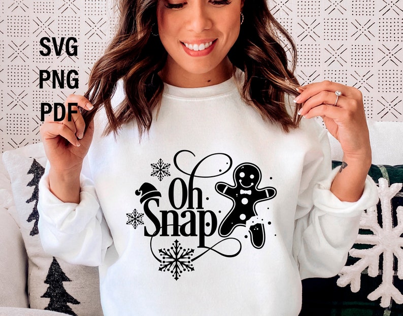 May include: White sweatshirt with black text that says "Oh Snap" and a gingerbread man graphic. The gingerbread man is wearing a red Santa hat.