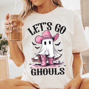 Może przedstawiać: Biała koszulka z nadrukiem ducha w r&oacute;żowym kowbojskim kapeluszu i butach. Na koszulce widnieje napis "Let's Go Ghouls".