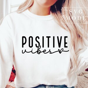 Peut inclure: Sweat-shirt blanc avec un texte noir qui dit "POSITIVE vibes" avec un petit symbole de c&oelig;ur.