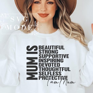 Op de afbeelding: Wit sweatshirt met zwarte tekst die "Moeder is" luidt en positieve eigenschappen van een moeder opsomt, waaronder mooi, sterk, ondersteunend, inspirerend, toegewijd, attent, onbaatzuchtig en beschermend. De tekst eindigt met "Ik ben moeder."