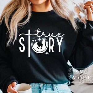 May include: A black sweatshirt with a white graphic design that says "true story" with a cross and a nativity scene inside a circle.