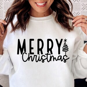 Puede incluir: Sudadera blanca con la frase "MERRY Christmas" en negro y un &aacute;rbol de Navidad estilizado. El texto est&aacute; en negrita. La sudadera es de manga larga y cuello redondo.