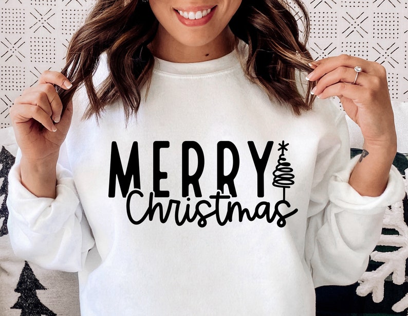 Puede incluir: Sudadera blanca con la frase "MERRY Christmas" en negro y un &aacute;rbol de Navidad estilizado. El texto est&aacute; en negrita. La sudadera es de manga larga y cuello redondo.