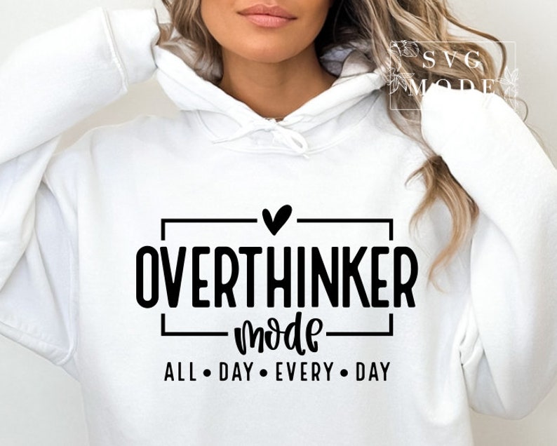 May include: White hoodie with the text "OVERTHINKER mode ALL DAY EVERY DAY" in black. The design includes a heart symbol above the word "OVERTHINKER". The hoodie has a drawstring hood and long sleeves.