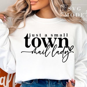 Peut inclure: Sweat-shirt blanc avec un texte noir qui dit "Just a small town mail lady" avec un petit c&oelig;ur.
