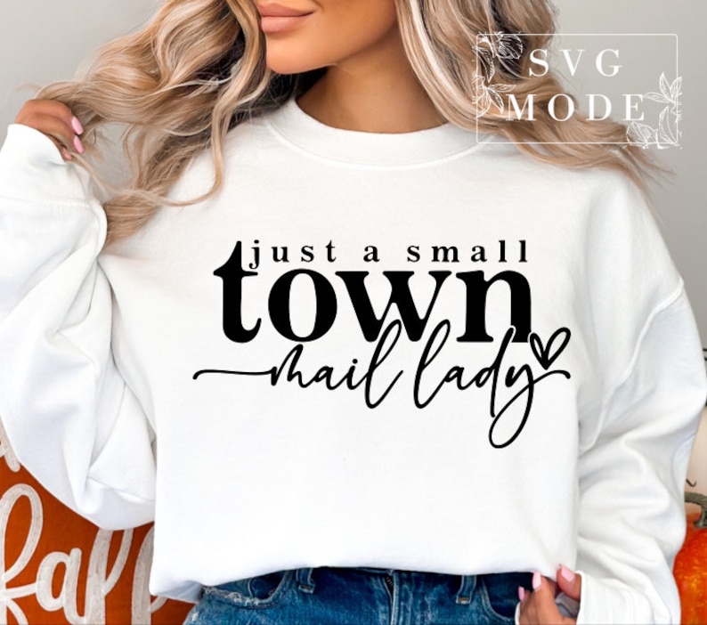 Peut inclure: Sweat-shirt blanc avec un texte noir qui dit "Just a small town mail lady" avec un petit c&oelig;ur.