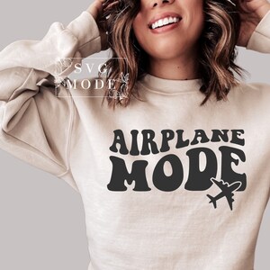 Puede incluir: Una sudadera beige con el texto "AIRPLANE MODE" en letras retro negras. Un peque&ntilde;o icono de avi&oacute;n est&aacute; a la derecha del texto.