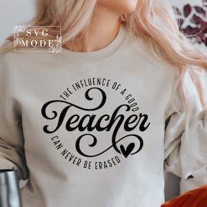 May include: A white sweatshirt with black text that reads "The influence of a good teacher can never be erased". The text is in a cursive font and includes a small heart.