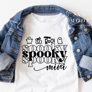 Puede incluir: Camiseta blanca con un dise&ntilde;o gr&aacute;fico negro que dice "spooky mini" con fantasmas, calabazas y murci&eacute;lagos alrededor del texto.