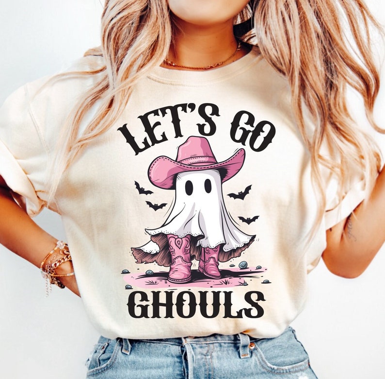 Może przedstawiać: Biała koszulka z nadrukiem ducha w r&oacute;żowym kowbojskim kapeluszu i r&oacute;żowych kowbojskich butach. Na koszulce widnieje napis "Let's Go Ghouls".