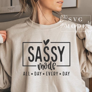 May include: A beige sweatshirt with the text "SASSY mode ALL DAY EVERY DAY" in black lettering. A small heart is above the word "SASSY".