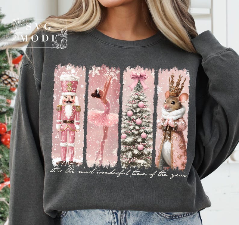 K&ouml;nnte beinhalten: Ein dunkelgrauer Pullover mit einem abgenutzten Design im Vintage-Stil, das einen rosafarbenen Weihnachtsbaum, eine Ballerina, einen Nussknacker und eine Maus mit Krone zeigt. Der Text "It's the most wonderful time of the year" ist unter dem Design gedruckt.